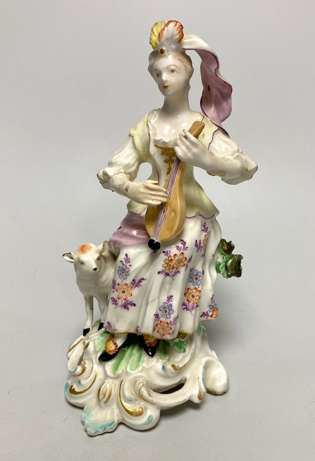 A Derby porcelain figure, modelled as a shepherdess playing a mandolin, seated on a stump, 18th century, 18cm high